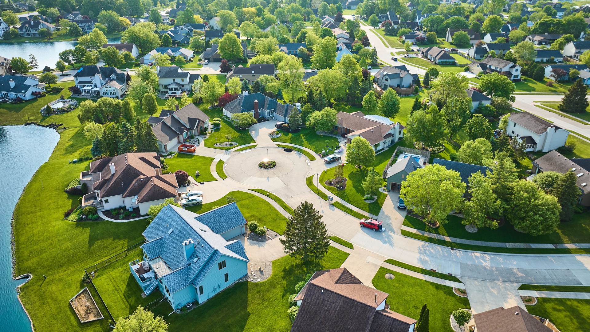 Cul-de-sac with large to middleclass homes in neighborhood with pond in summertime aerial